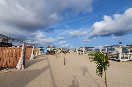 Rolling white waves crashing onto the wide golden sand shoreline of Elegushi Beach in Lekki, Lagos, featuring private beach lounges and palm trees.